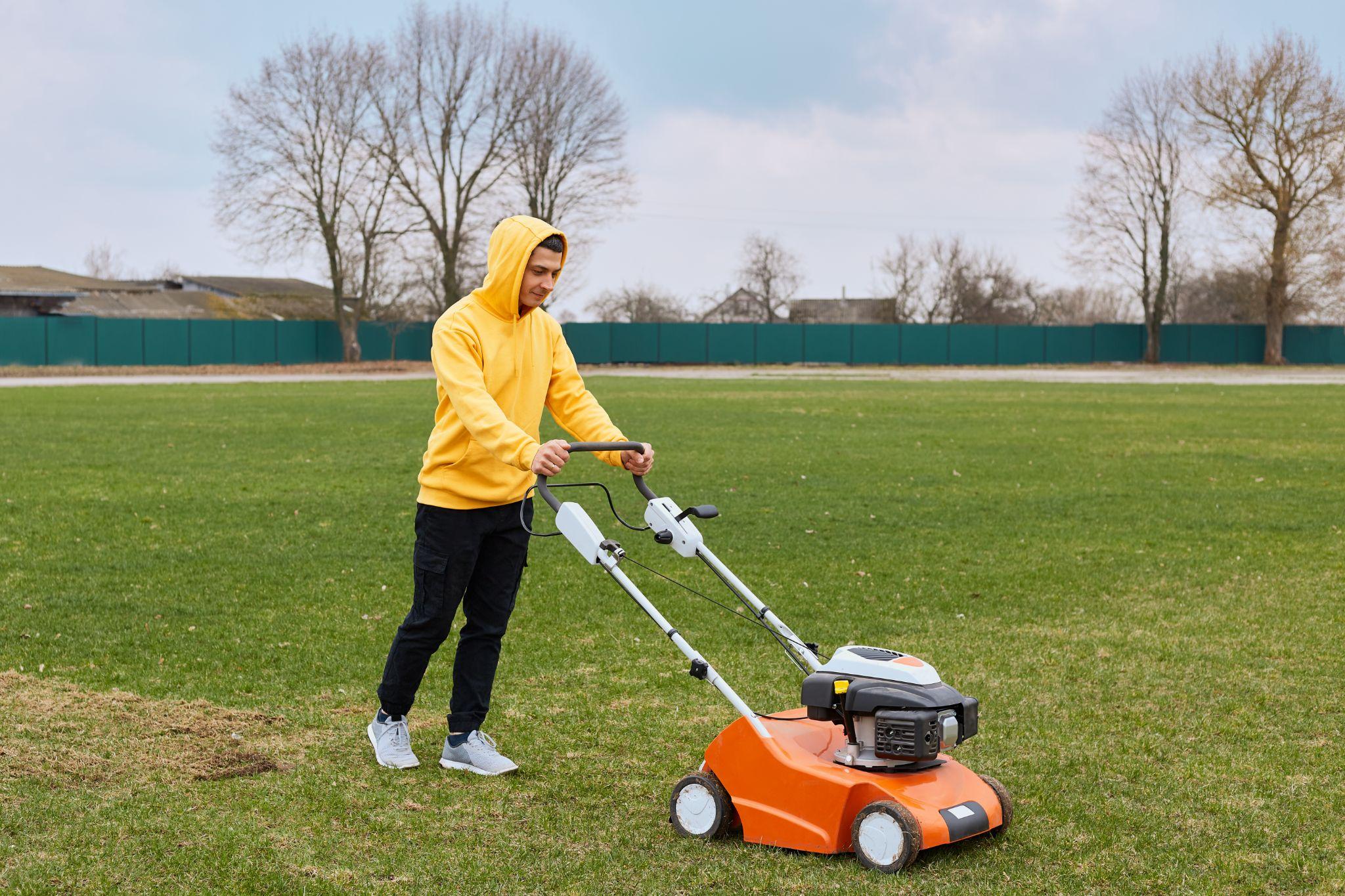 Man in a yellow hoodie mowing a large grassy field with an orange lawn mower.